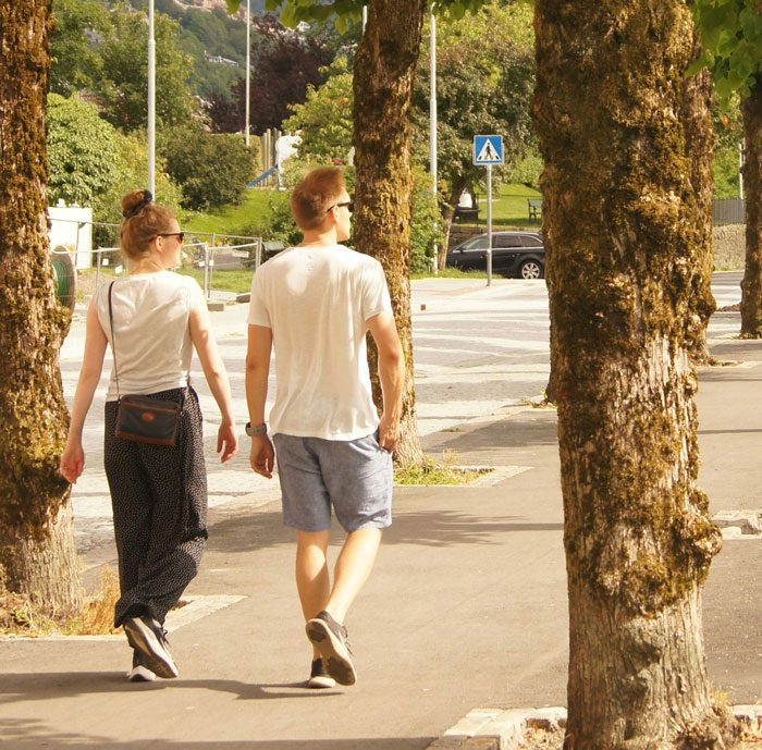 Two Americans walking on a tree-lined street abroad, showcasing behaviors that make them stand out in a foreign country.