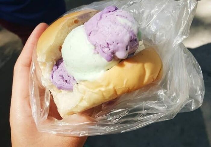 Hand holding ice cream sandwich with purple and white ice cream in a bun, example of food nobody should eat for health.