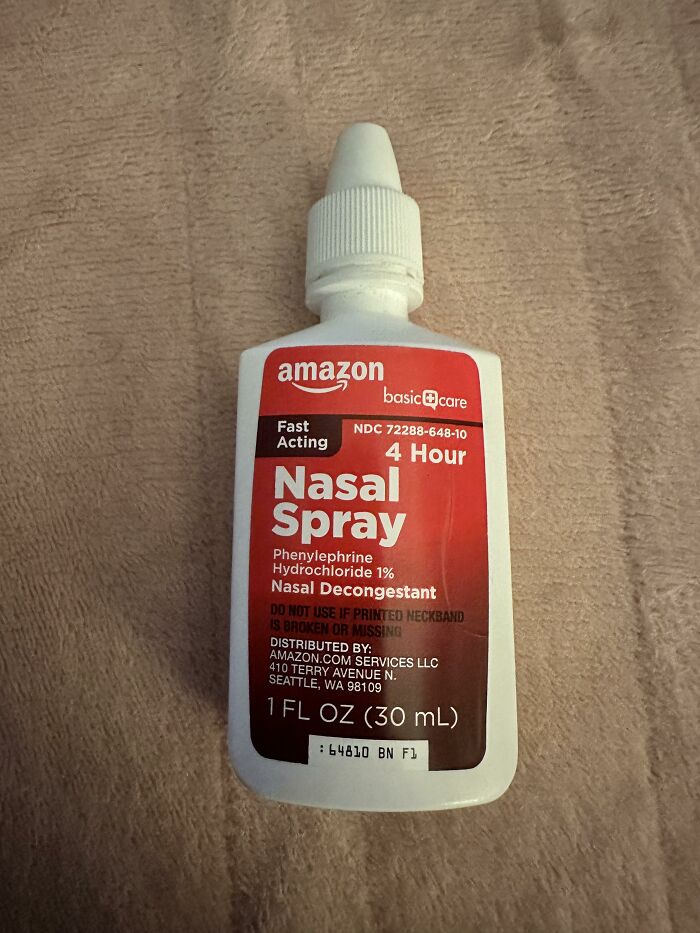 Amazon basic care nasal spray bottle on a beige surface, highlighting fast acting 4-hour nasal decongestant relief.