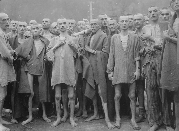 Emaciated men in worn clothing gather closely in a haunting historical photo from a concentration camp during World War II.