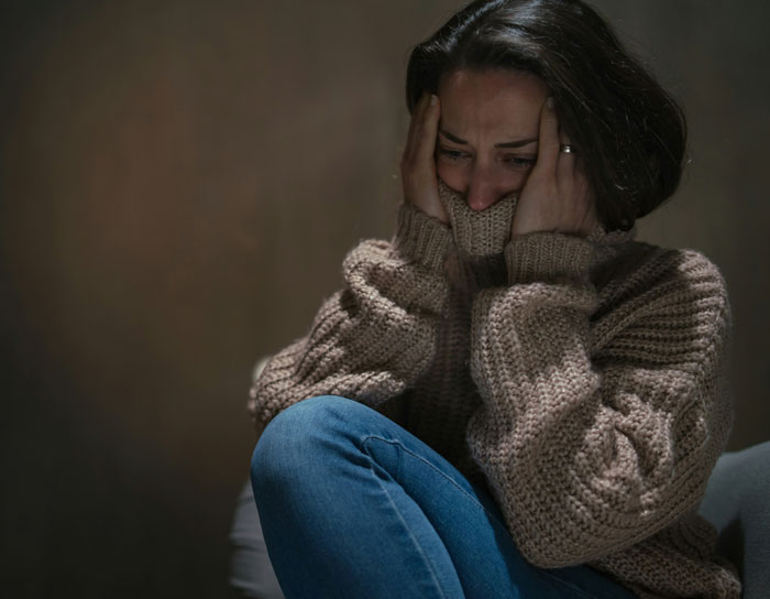 Woman sitting worried and scared in a dark room, illustrating fear after a dog attacks stalker who broke into home. Woman sitting worried and scared in a dark room, illustrating fear after a dog attacks stalker who broke into home.
