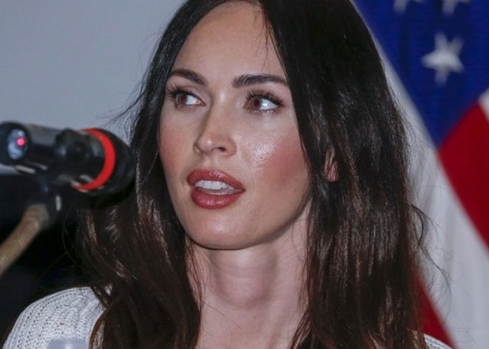 Actress speaking into microphone with American flag in background, sharing a total gentleman celebrity encounter.