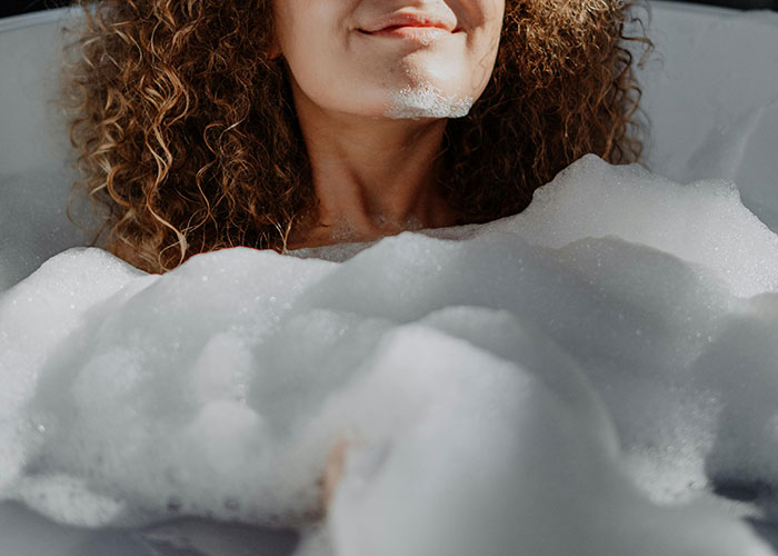 Young woman with curly hair relaxing in a bubble bath, illustrating wild and embarrassing drinking stories concept.