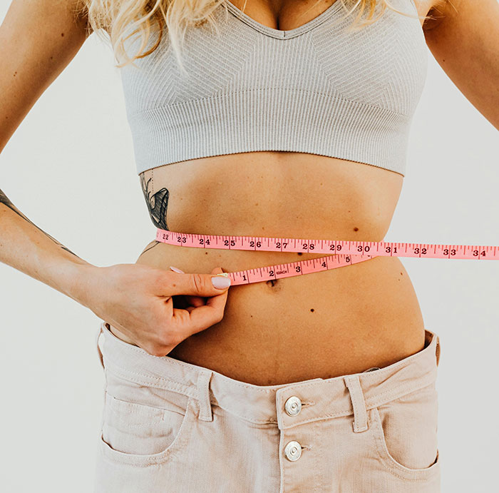 Woman measuring waist with pink tape measure, symbolizing weight loss related to Ozempic vulva side effects.