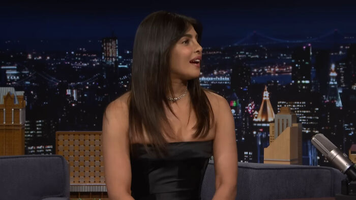 Celebrity in a black dress on a late-night talk show set discussing Hollywood leading A-listers and audience reception.