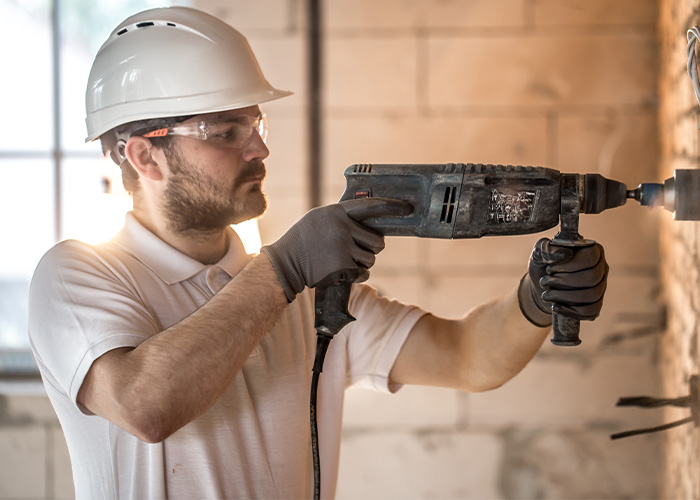 Man wearing safety gear using power drill on construction site, illustrating common causes of house fires including accidents.
