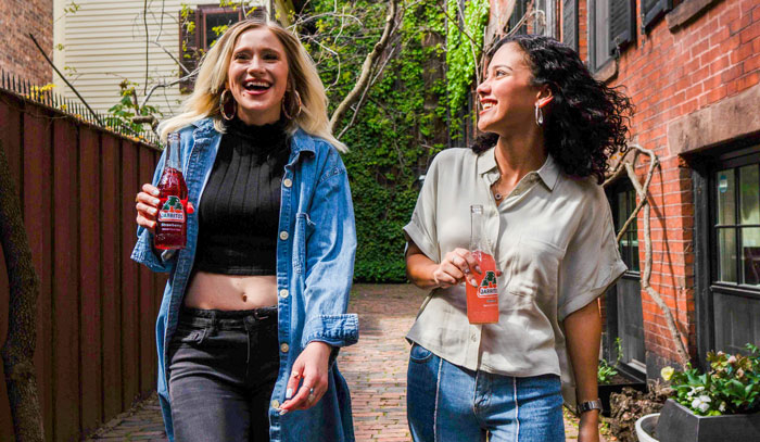 Two women smiling and holding beverages outdoors, illustrating things Americans do that make them stand out abroad.