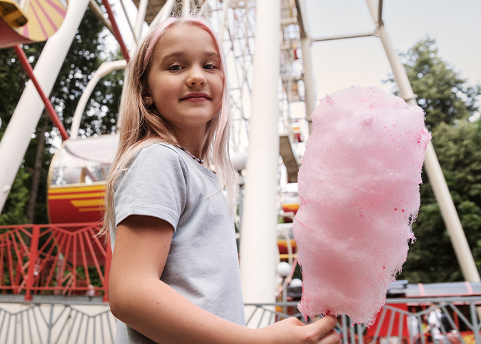 Young girl enjoying cotton candy at an amusement park, reflecting moments when rich people realize different lifestyles. - 13