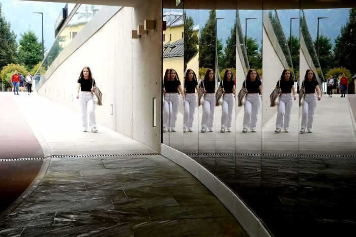 Woman walking past reflective mirrored wall on street, capturing unseen, unposed moments in street photography.