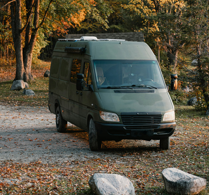Green work van parked on a leaf-covered driveway with professionals who work in other people’s homes nearby in autumn.