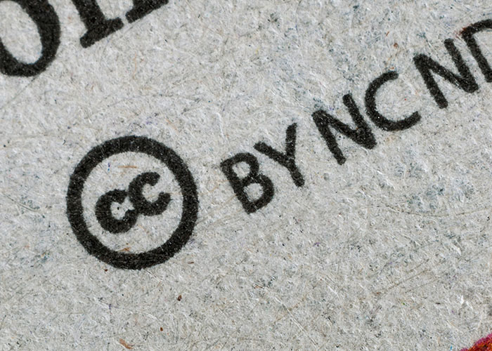 Close-up of a Creative Commons license symbol printed on textured paper showing common illegal actions like driving over the speed limit.