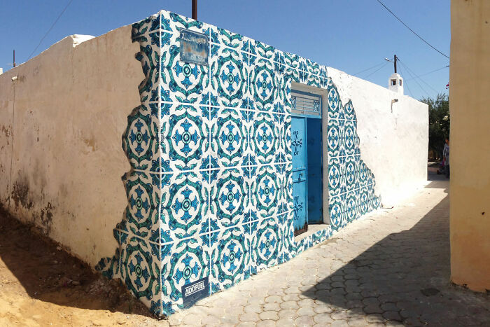 Blue and white geometric street art painted on a corner wall with a blue door under a clear sky