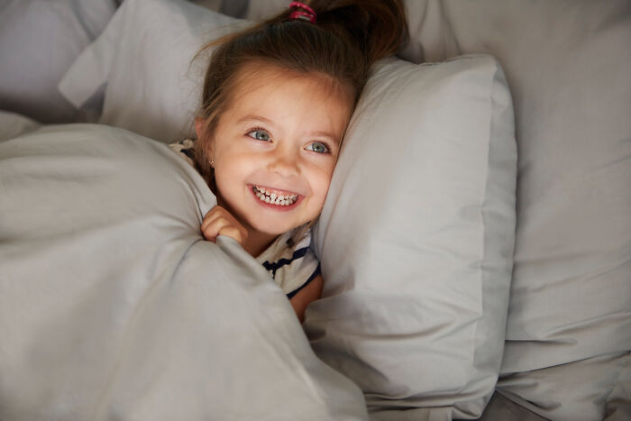 Smiling child lying in bed under covers, evoking feelings related to the scariest sounds ever heard by people at night.
