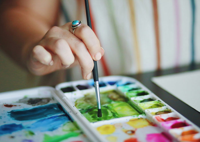 Close-up of a hand holding a paintbrush over a colorful palette, illustrating creative and unhinged wedding spends. - 5