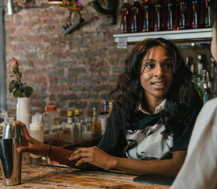 Bar staff bartender engaging with a customer behind the counter in a cozy bar setting protecting women from creeps.