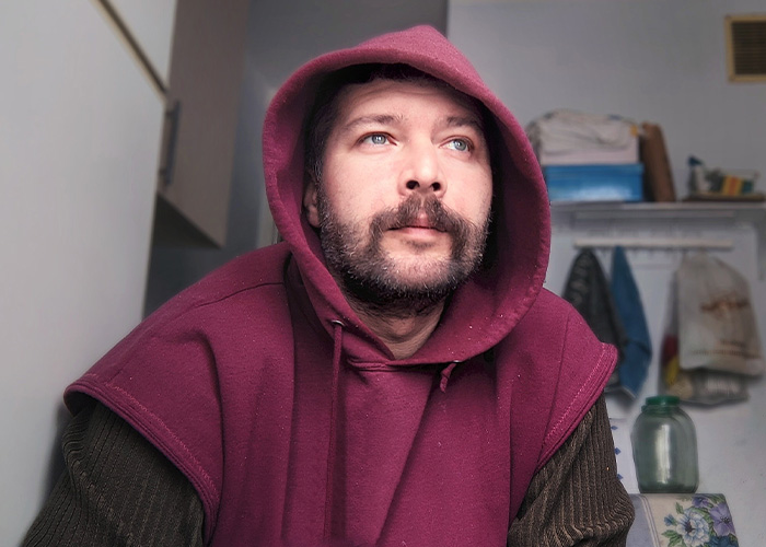 Man wearing a maroon hoodie looking thoughtful indoors, illustrating careless causes of house fires including Roomba accidents.