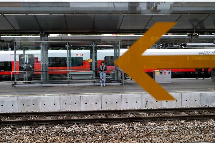 Person waiting at a train station, captured in an unseen, unposed moment on the streets by a photographer.