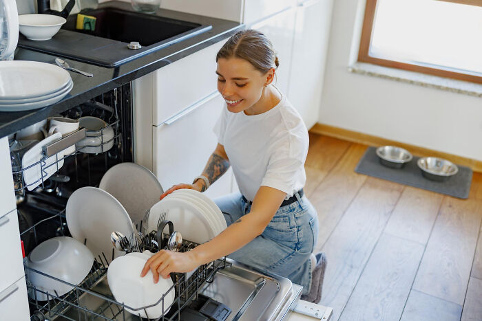 Woman loading dishwasher in a bright kitchen, demonstrating a low effort high reward household task.
