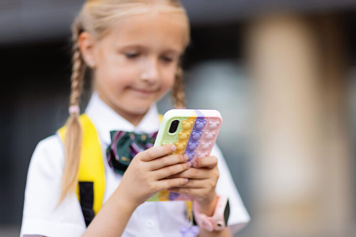 Young school kid confidently using a smartphone with a colorful pop-it case outdoors, showcasing wild creativity and confidence.