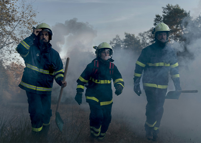 Three firefighters in protective gear walking through smoke during a house fire emergency response.
