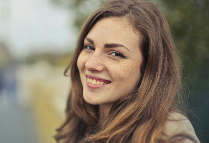 Young woman with freckles smiling outdoors, representing things Americans do that make them stand out in a foreign country