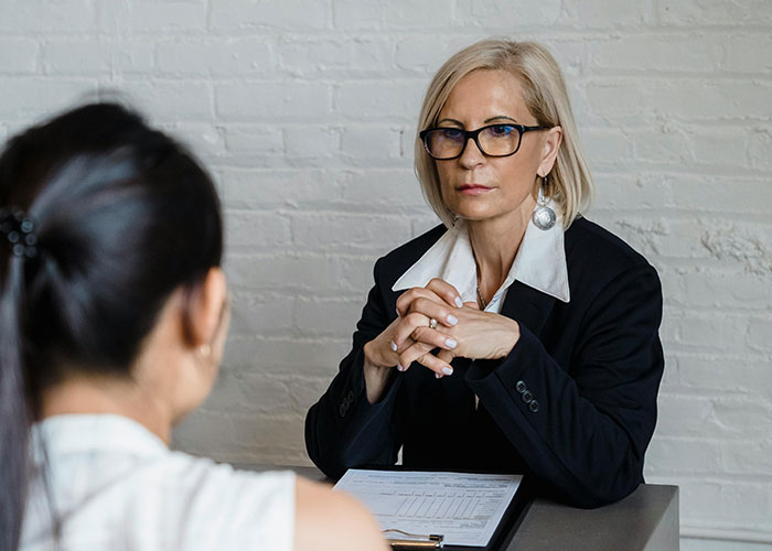 A serious professional woman in glasses interviewing a candidate, illustrating jobs that only a person without a soul would do.
