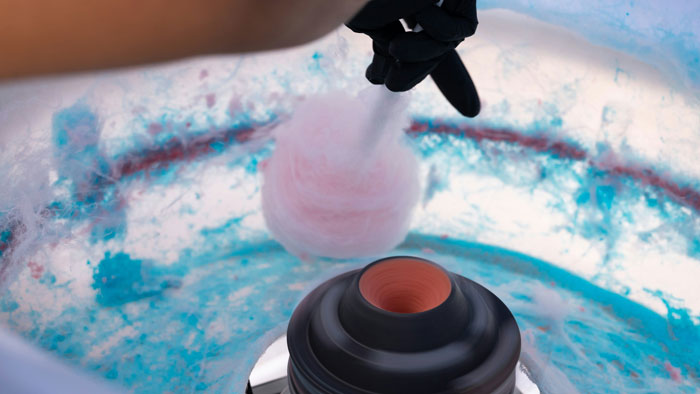 Hand in black glove preparing pink cotton candy using a spinning machine, illustrating unhinged wedding spends. - 14
