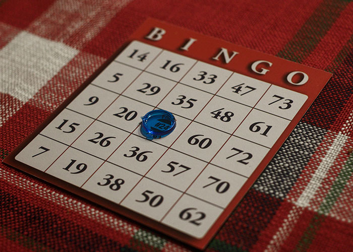 Bingo card on a red plaid tablecloth with a blue marker, illustrating wild and embarrassing drinking stories concept.