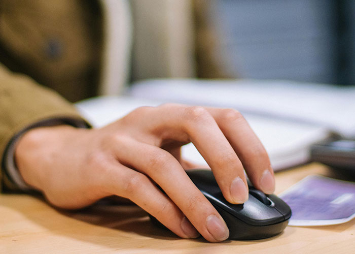 Close-up of a person’s hand using a computer mouse while researching drive over the speed limit topics online.