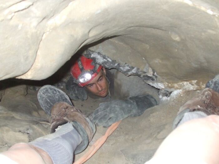 A man wearing a red helmet with a headlamp crawls through a narrow cave passage in a terrifying true story.