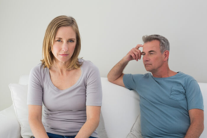 Young woman and middle-aged man sitting apart on couch, reflecting strained stepdad and stepdaughter relationship conflict.