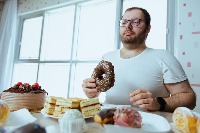 Man wearing glasses sitting at a table with various desserts, highlighting non-substance dependencies including shopping.