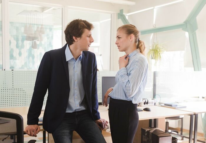 A young man using smooth pickup lines while talking to a woman in a modern office setting.