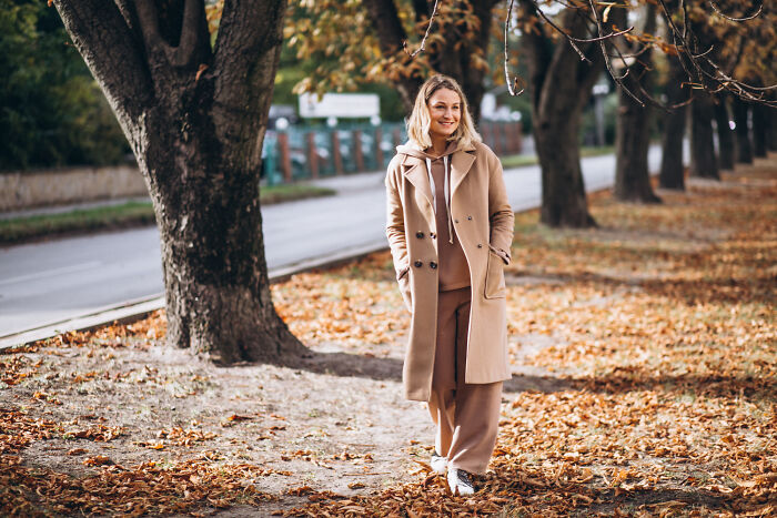 Woman in a beige coat walking outdoors in autumn, representing low effort high reward lifestyle tips in nature.
