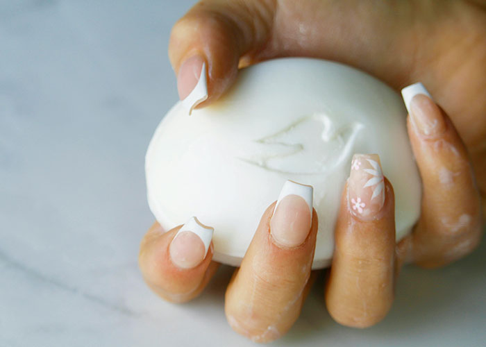 Close-up of hands with decorated nails holding a white bar of soap, symbolizing wild and embarrassing drinking stories.