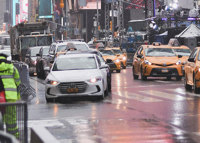 City street traffic with multiple cars and taxis driving over the speed limit on a wet road during rush hour.