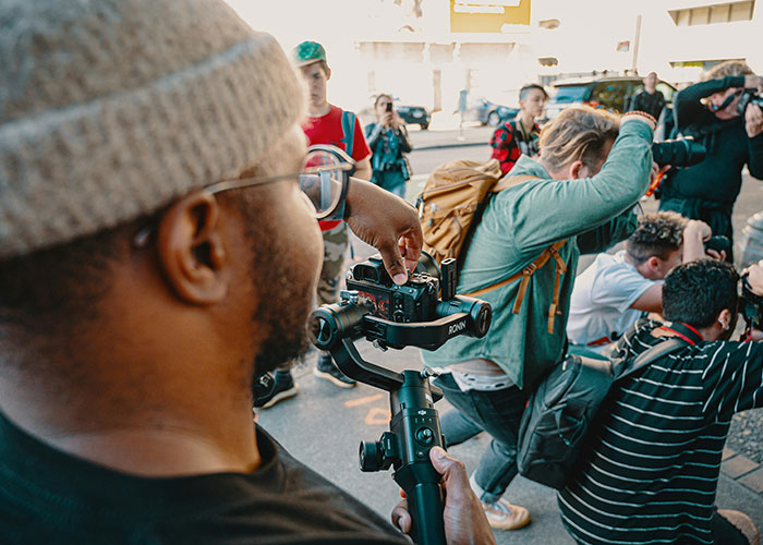 Photographer capturing images with a camera on a stabilizer among a group of people outdoors, highlighting jobs without a soul.