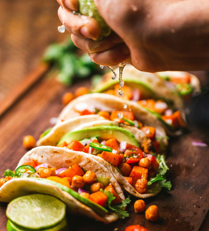 Close-up of tacos with chickpeas and vegetables being squeezed with fresh lime, illustrating unhinged wedding spends on food. - 9
