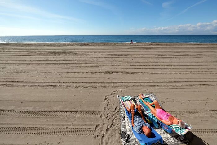 Two people relaxing on a nearly empty beach, capturing life’s unseen, unposed moments on the streets by a photographer.