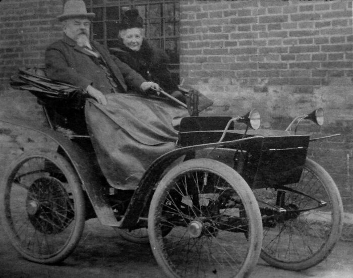 Early 20th century vintage car with an elderly couple seated, showcasing how wild the first cars really were 100 years ago.