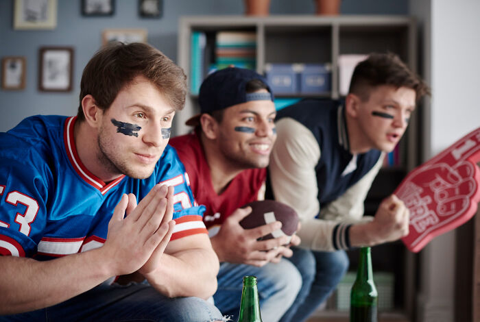 Three men with face paint, watching a game intensely, showcasing fan excitement and shopping for sports gear.