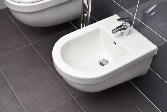 White bidet with modern faucet installed in bathroom with dark tiles, illustrating low effort high reward hygiene solution.