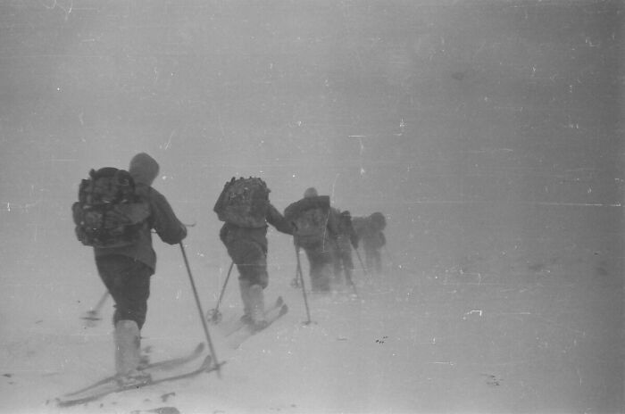 Group of people skiing through a harsh snowstorm, capturing a creepy and unsettling moment in low visibility conditions.