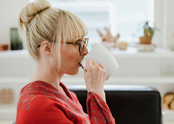 Woman wearing glasses and a red sweater enjoying a quiet moment with a cup of coffee during a family treats wedding occasion.