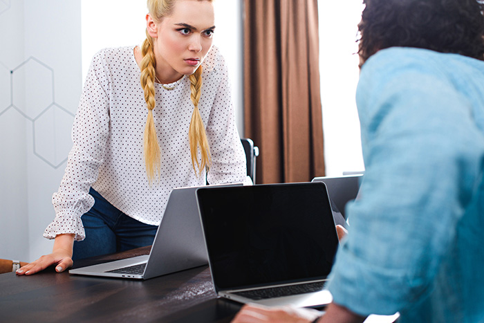 Two coworkers engaged in a tense discussion at a desk with laptops, illustrating workplace conflict and HR concerns.