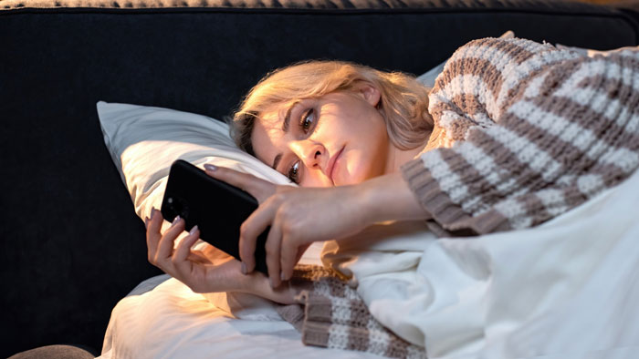 Woman lying in bed looking at her phone, reflecting on man orders wife to get a job if she wants allowance Woman lying in bed looking at her phone, reflecting on man orders wife to get a job if she wants allowance