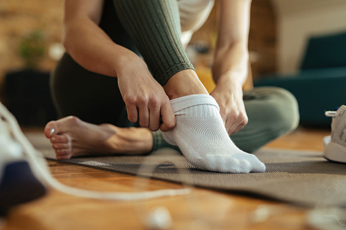 Woman putting on mysterious white sock at home, focusing on foot and hand in cozy indoor setting.