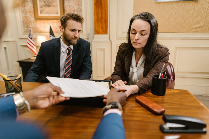 Man and woman in formal attire sitting at a desk discussing a document about family and marriage issues.