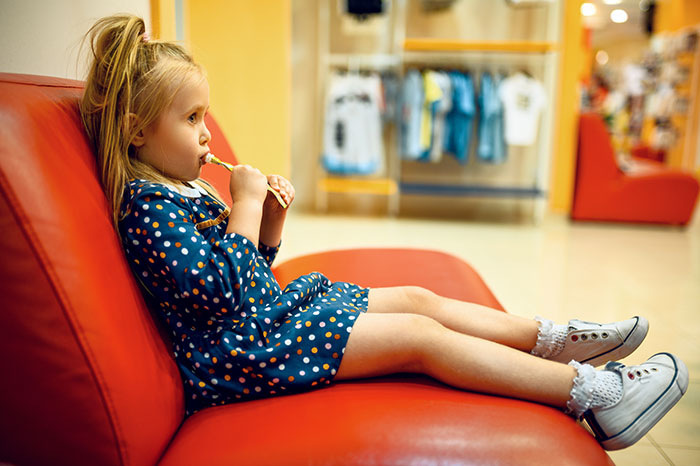 Toddler niece in a blue polka dot dress sitting on a red couch while waiting during a doctor appointment with her uncle.