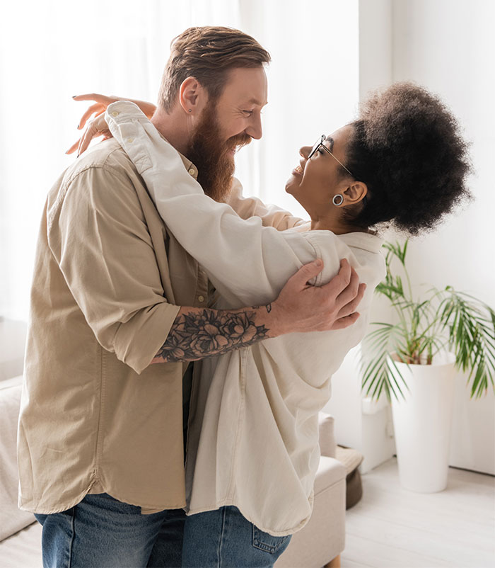 Couple embracing and smiling indoors, woman showing shock and surprise about brother’s wife nicknames being cruel. Couple embracing and smiling indoors, woman showing shock and surprise about brother’s wife nicknames being cruel.